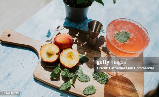 a peach flavoured drink sits on a wooden chopping board with fresh fruit - menta gastronomía fotografías e imágenes de stock