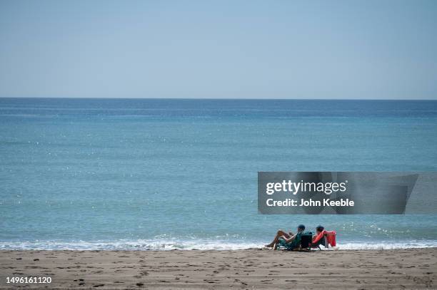 Couple relax and sunbath in deckchairs close to the sea on the beach on a clear blue sky sunny day on April 20, 2023 in Malaga, Spain.