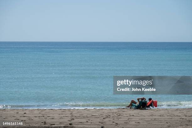 Couple relax and sunbath in deckchairs close to the sea on the beach on a clear blue sky sunny day on April 20, 2023 in Malaga, Spain.