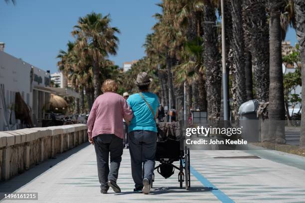 An elderly woman is helped as she walks along the promenade by the beach on April 20, 2023 in Malaga, Spain.