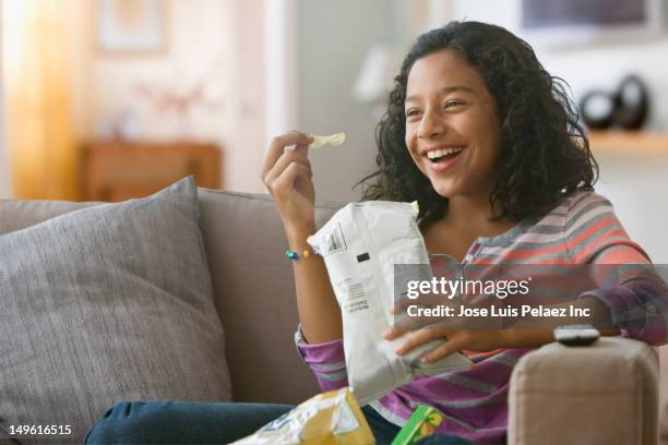 hispanic girl eating potato chips on sofa - bag of potato chips stockfoto's en -beelden