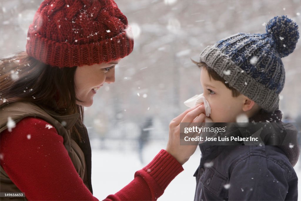 Caucasian mother wiping son's nose in the snow