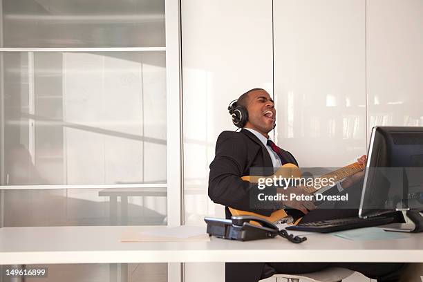 black businessman playing guitar at desk - eskapismus stock-fotos und bilder