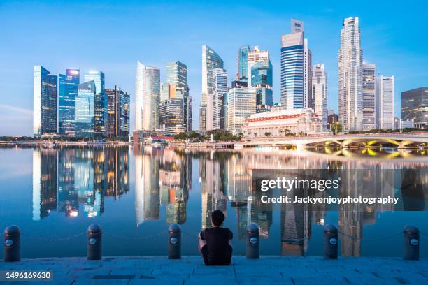 the young man sat and stand on the dock with urban skyline and skyscrapers in marina bay singapore. - singapore financial district stock-fotos und bilder