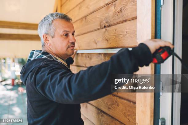 measuring the woodwork: mature builder using a tape measure near wooden house outdoors - longitud fotografías e imágenes de stock