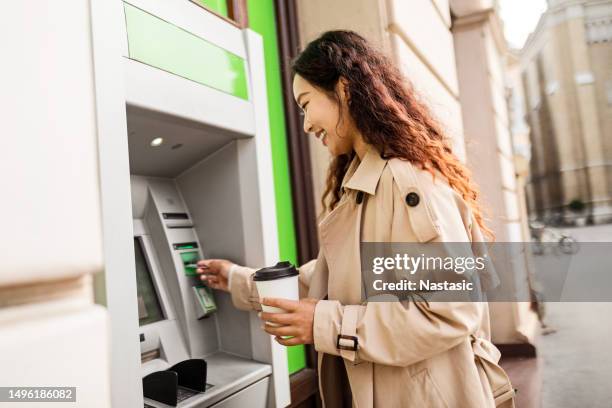 young girl with coffee cup withdrawing money at atm - first-atm-machine stock pictures, royalty-free photos & images