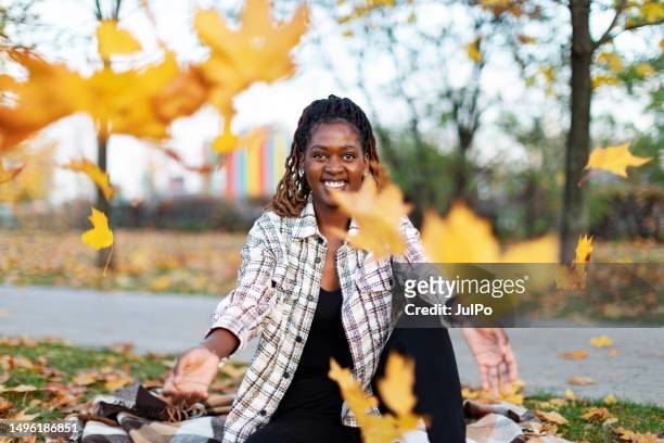 young adult black female throwing maple leaves in park - november stockfoto's en -beelden