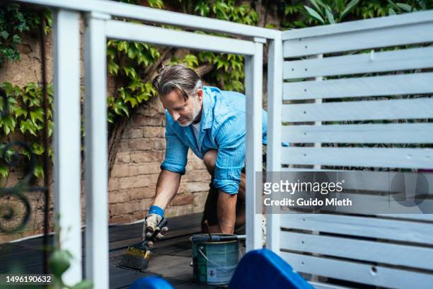 man preparing wooden deck with organic oil at home. - nägel stock-fotos und bilder