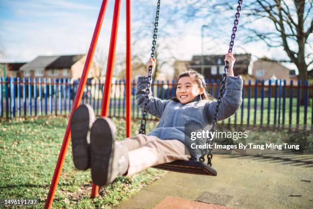 lovely cheerful girl playing on a swing set in playground joyfully - swinging stock pictures, royalty-free photos & images