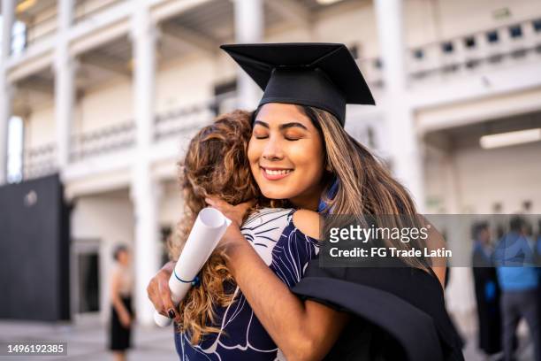joven graduada abrazando a su madre en la graduación - alumni fotografías e imágenes de stock