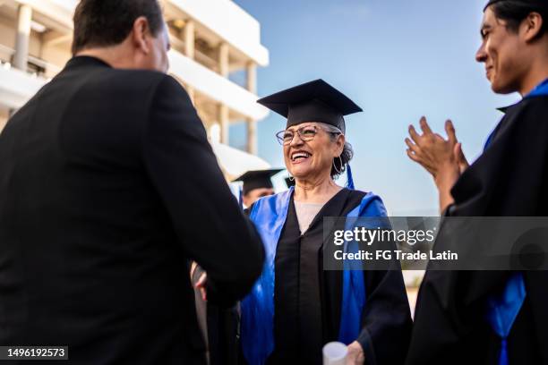 senior graduate woman receiving her diploma on graduation - graduation gown stock pictures, royalty-free photos & images