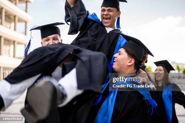 young man being thrown up by his friends while celebrating on graduacion - graduacion stock pictures, royalty-free photos & images