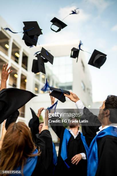 giovani laureati lanciano il loro mortaio in aria mentre festeggiano la laurea - celebrazione della laurea foto e immagini stock