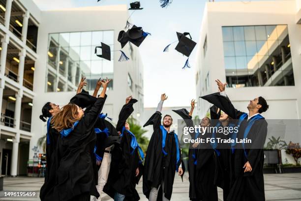 young graduates throwing their mortarboard in the air while celebrating on graduation - graduation excitement stock pictures, royalty-free photos & images