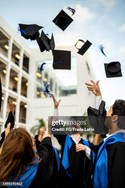 young graduates throwing their mortarboard in the air while celebrating on graduation - arremessar imagens e fotografias de stock