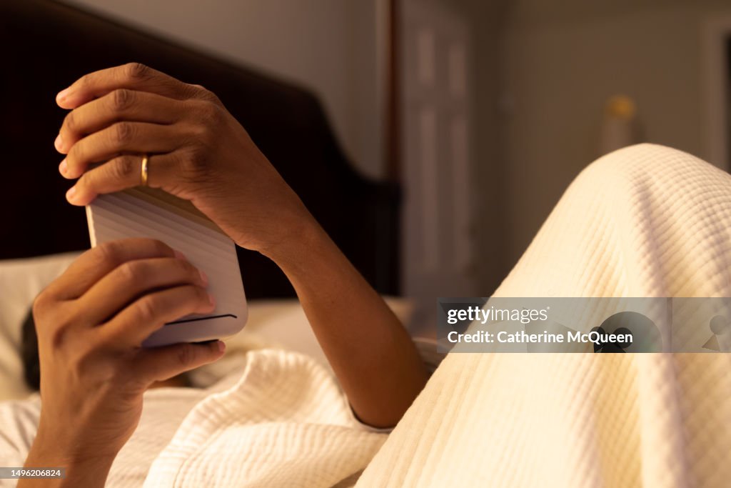 Black woman using smart phone in bed