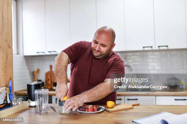 balding male squeezing lemons in kitchen - fat nutrient stock pictures, royalty-free photos & images
