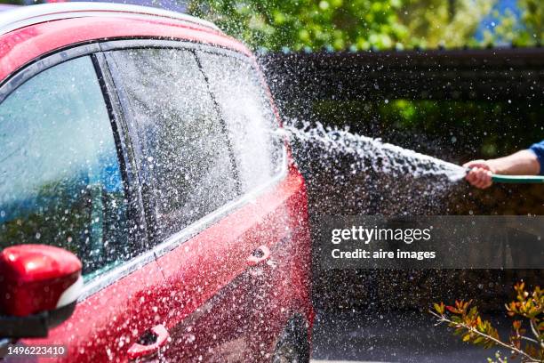 side view of a woman's hand standing holding a hose washing a car with water in the garage. - manguera fotografías e imágenes de stock