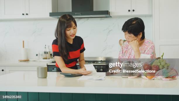 young asian woman and her mother sorting out payment bills and household finances in the kitchen, inflation, high cost of living concept - energy bill stock pictures, royalty-free photos & images