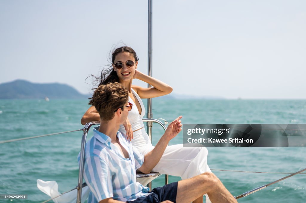 Caucasian romantic couple looking at beautiful view during yachting. Attractive young man and woman hanging out celebrating anniversary honeymoon trip while catamaran boat sailing during summer sunset