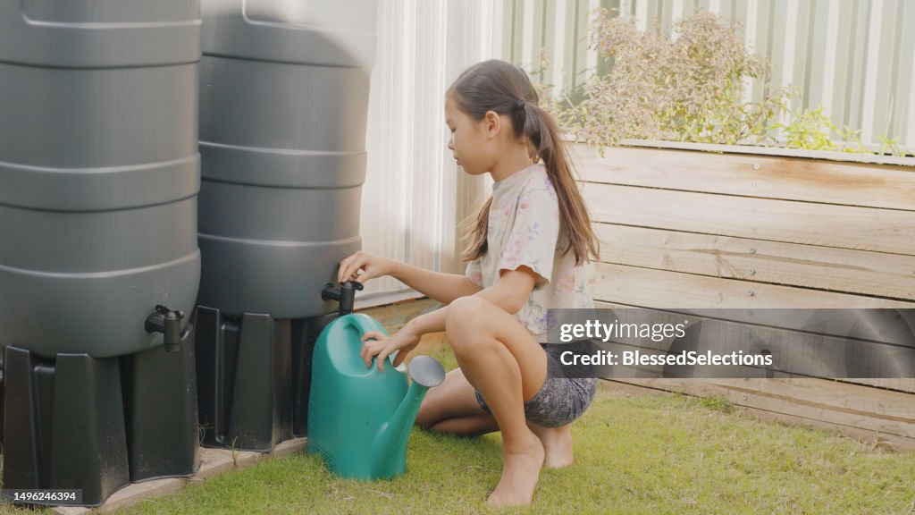 Mixed preteen girl getting water from rainwater butt for watering homegrown produce at home, sustainable living lifestyle concept
