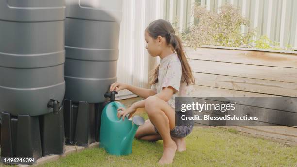 mixed preteen girl getting water from rainwater butt for watering homegrown produce at home, sustainable living lifestyle concept - rainwater tank stock pictures, royalty-free photos & images