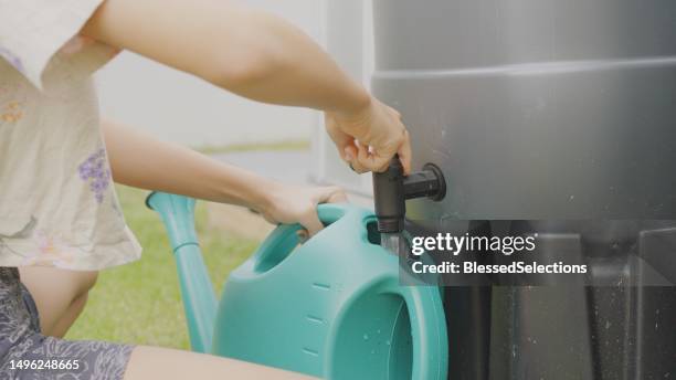 préadolescente mixte obtenant de l’eau de pluie pour arroser les produits cultivés à la maison, concept de mode de vie durable - réservoir de stockage photos et images de collection