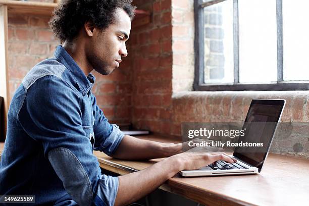 young guy using laptop at desk - type stock pictures, royalty-free photos & images