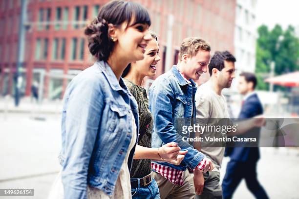 four young adults crossing city street - kleine personengruppe stock-fotos und bilder
