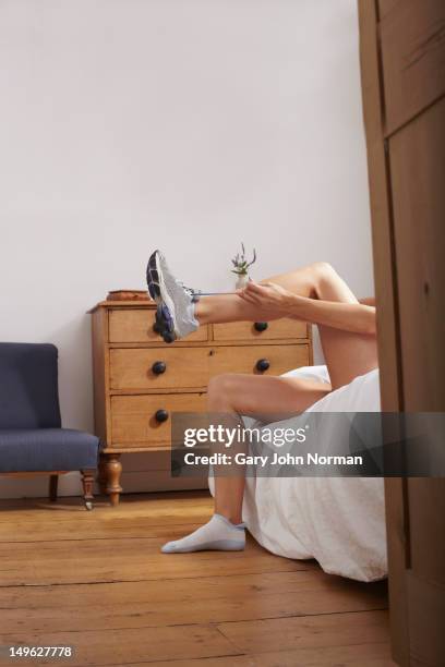 woman sitting on bed putting on trainers. - legs on the table stock pictures, royalty-free photos & images