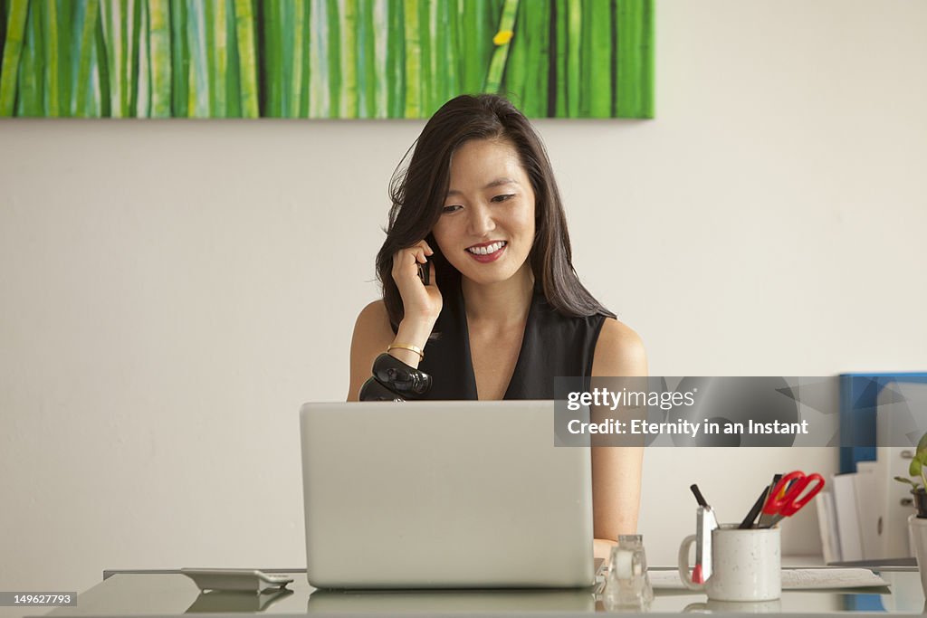 Asian businesswoman on phone looking at computer