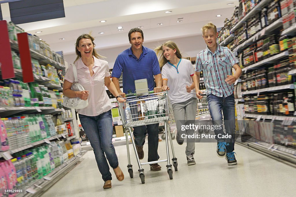 Family running in supermarket aisle with trolly