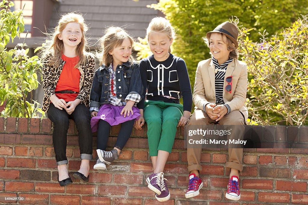 Four smiling kids sitting on a brick wall.