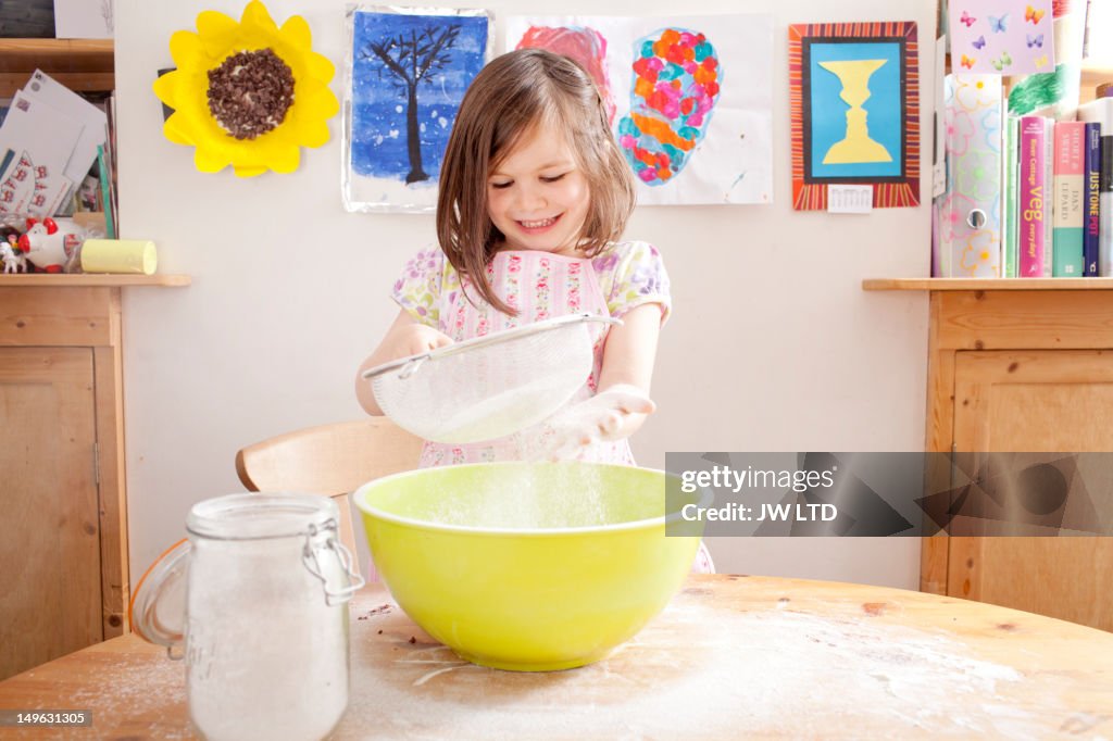 Girl (4-5) sifting flour