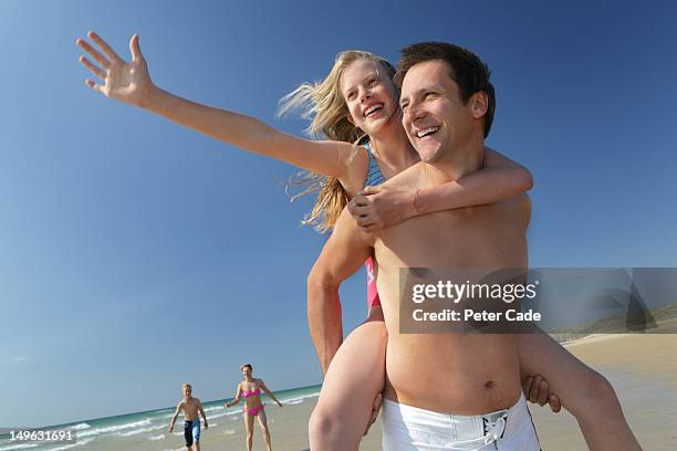 family on beach, father-daughter piggback - summer fun stock pictures, royalty-free photos & images