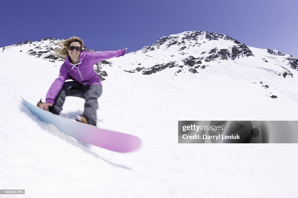 Young female snowboarder carving down snowy slope.