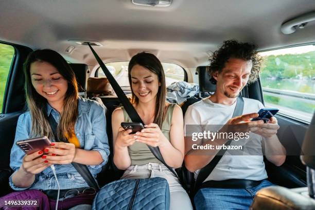 three friends using their phones while riding in the backseat of the car - comfortable car stock pictures, royalty-free photos & images