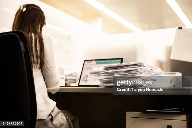 a pile of papers placed next to a woman working overtime. - trabajar demasiado fotografías e imágenes de stock