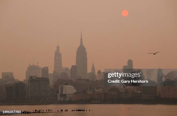 The sun is shrouded as it rises in a hazy, smokey sky behind the Empire State Building, One Vanderbilt and the Chrysler Building in New York City on...