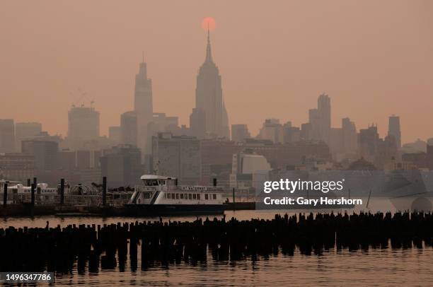 The sun is shrouded as it rises in a hazy, smokey sky behind the Empire State Building, One Vanderbilt and the Chrysler Building in New York City on...