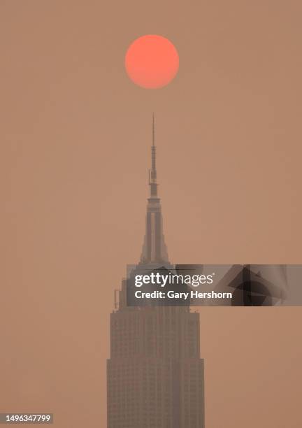The sun is shrouded as it rises in a hazy, smokey sky behind the Empire State Building in New York City on June 6 as seen from Jersey City, New...