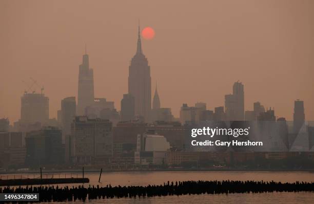 The sun is shrouded as it rises in a hazy, smokey sky behind the Empire State Building, One Vanderbilt and the Chrysler Building in New York City on...