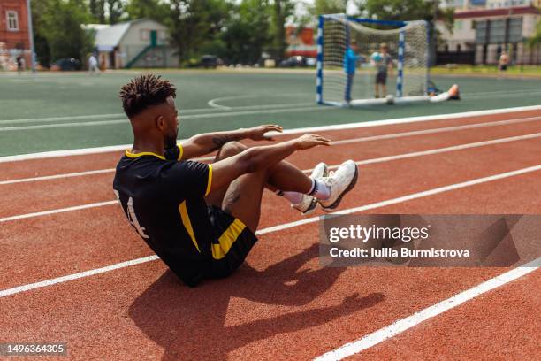 athletic young man of west asian ethnicity warming up abdomen muscles doing elevated sit-ups on racetrack near soccer field - west course stock pictures, royalty-free photos & images