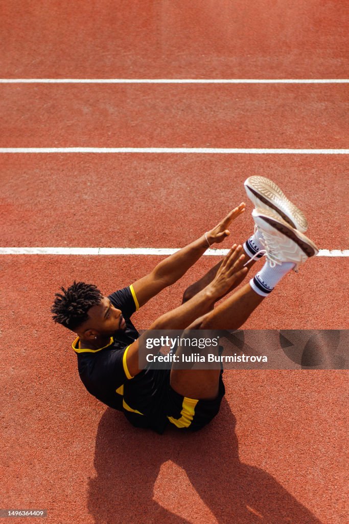 Young professional sportsman of Iranian ethnicity doing elevated crunches with lifted hands and legs in sports venue