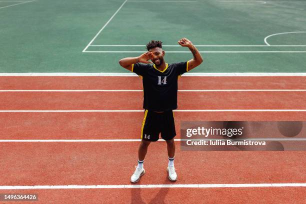 young male athlete of west asian ethnicity standing on red running track with arms raised smiling - west course stock pictures, royalty-free photos & images