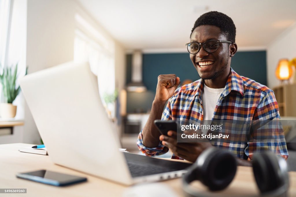 Male African-American student celebrating exam pass, after he saw exam result on laptop