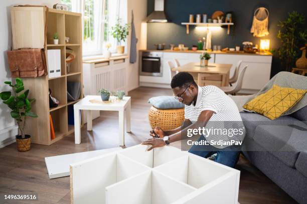 african-american man using electric screwdriver while assembling new furniture in the apartment - ikea furniture stock pictures, royalty-free photos & images