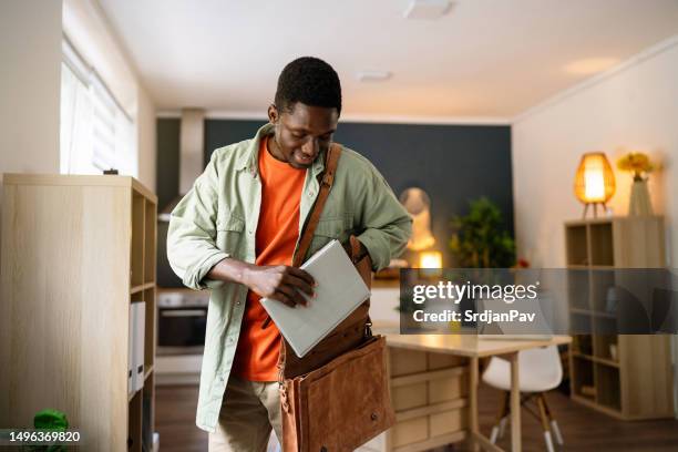 junger afroamerikanischer männlicher student steckt ein buch in eine ledertasche - ledertasche stock-fotos und bilder