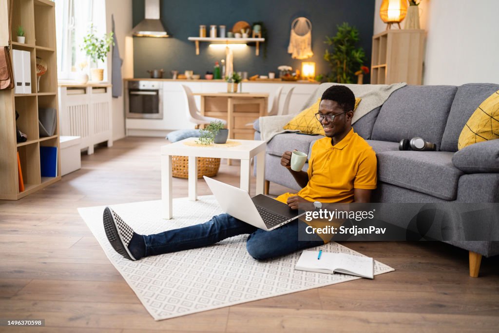 At his home, male African-American freelancer working on laptop while drinking coffee