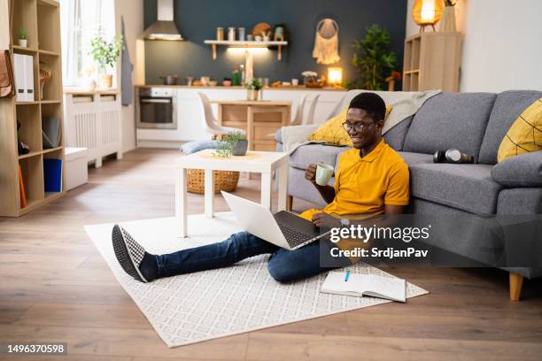 at his home, male african-american freelancer working on laptop while drinking coffee - yellow sofa stock pictures, royalty-free photos & images